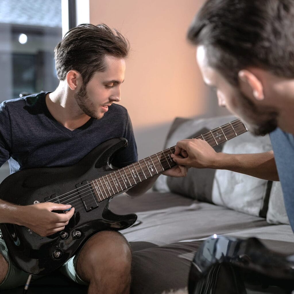 Professeur enseignant la guitare électrique à un adulte lors d'un cours à domicile.