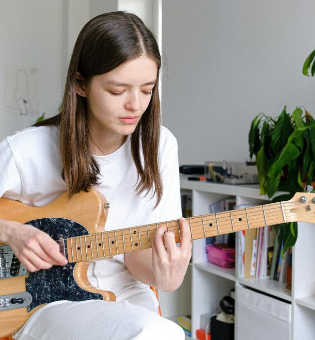 Adolescente qui apprend la guitare électrique à domicile avec son instrument dans une pièce lumineuse